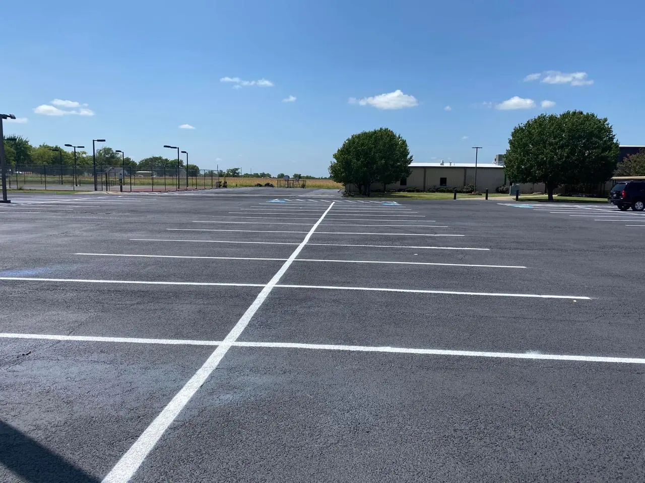 Wide asphalt parking area with white space markings and trees beyond